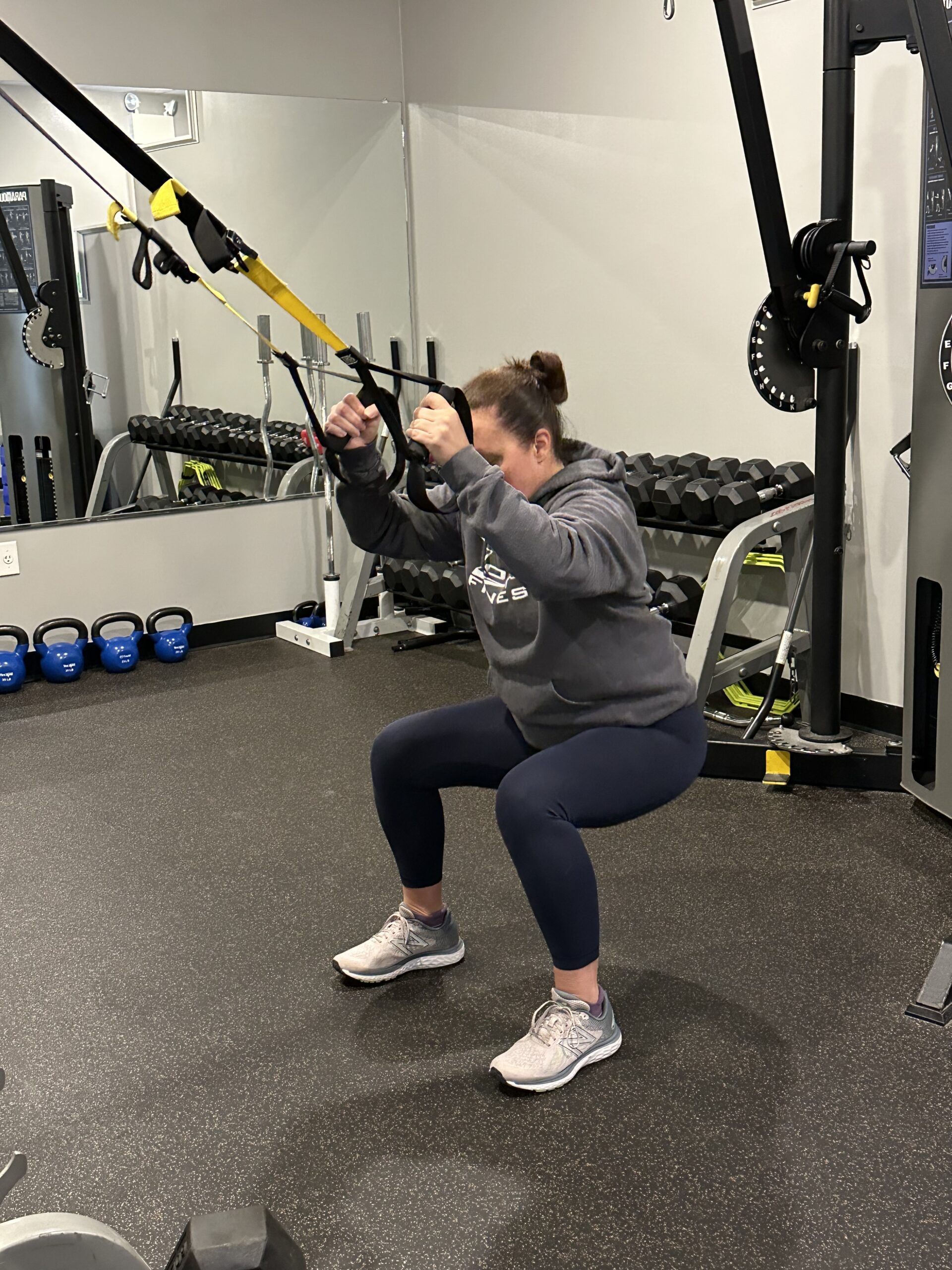 Female personal trainer demonstrating how to do a TRX squat.